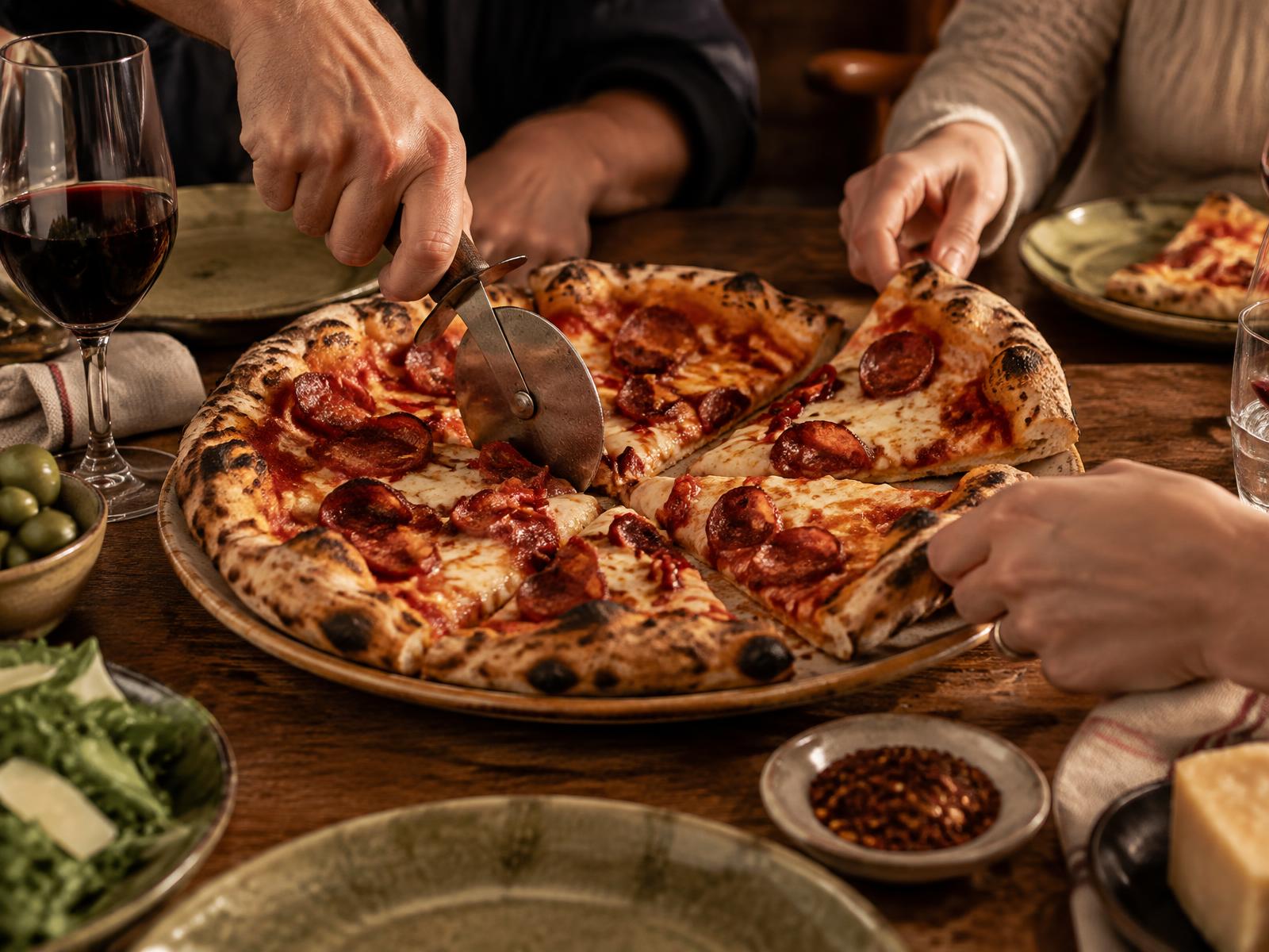 Pizza e ngrohtë duke u ndarë në tavolinë
